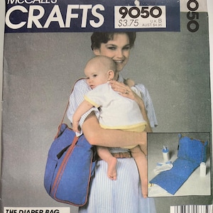 May include: A McCall's Crafts 9050 sewing pattern envelope for a blue diaper bag that converts into a changing station. The cover features a blue bag with brown trim, text describing its convertible shoulder and backpack functions, and an inset image showing the bag unfolded as a changing mat with baby care accessories.