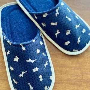Pu&ograve; includere: Un paio di pantofole blu e bianche con un motivo a coniglio. Le pantofole hanno un bordo bianco e una fodera morbida e confortevole.