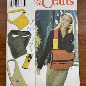 May include: A Simplicity Crafts 9000 sewing pattern envelope featuring illustrations and a photograph of various crossbody bags and pouches. The designs include a yellow sling bag, a dark green bag, a small yellow pouch, and a large orange messenger bag.