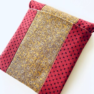 May include: A small, rectangular pouch made of fabric with a red and gold floral pattern. The pouch has a zipper closure and a white seam down the center.