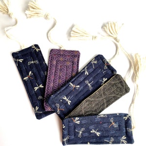 May include: Five fabric bookmarks with a dragonfly pattern. The bookmarks are in shades of blue, purple, and black. Each bookmark has a white tassel.