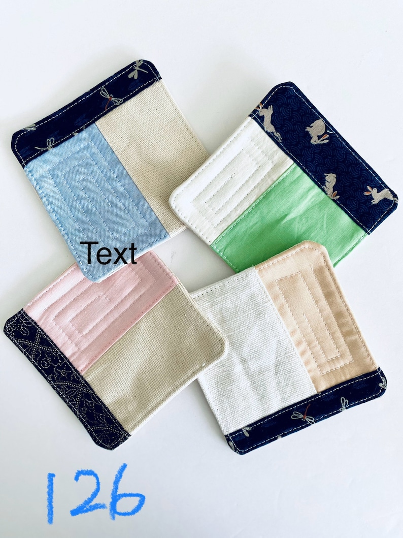 Pode incluir: Quatro bases de tecido quadradas com um design de patchwork. Cada base apresenta uma borda azul marinho com um padr&atilde;o de lib&eacute;lulas e se&ccedil;&otilde;es de tecido azul claro, branco, rosa e bege. A palavra "Text" &eacute; vis&iacute;vel em uma base e o n&uacute;mero "126" &eacute; vis&iacute;vel na parte inferior.