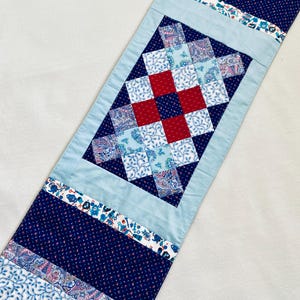 Pode incluir: Um corredor de mesa de patchwork azul e vermelho com um padr&atilde;o de diamante no centro. O corredor &eacute; feito de v&aacute;rios tecidos com desenhos florais e paisley.