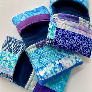 Puede incluir: Un conjunto de bolsas de tela hechas a mano en varios tonos de azul, turquesa y morado. Cada bolsa presenta diseños de patchwork únicos con patrones florales, de olas y geométricos. Las bolsas tienen un interior azul oscuro y probablemente se utilizan para guardar cosas.