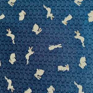 Peut inclure: Un tissu bleu avec un motif répétitif de lapins blancs et un motif de vague bleu.