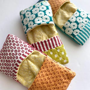 以下が含まれることがあります： カラフルなキルト生地のポーチのコレクション。各ポーチは、赤、黄、緑、青、オレンジの色合いの、花柄、ストライプ、水玉模様のユニークなパッチワークデザインが特徴です。ポーチは上部が開いており、対照的なインテリアが明らかになっています。