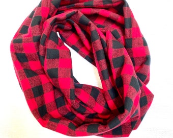 Könnte beinhalten: Ein roter und schwarzer Büffel-Plaid-Schal. Der Schal ist aus einem weichen Stoff gefertigt und ist so konzipiert, dass er um den Hals geschlungen getragen werden kann. Das Muster ist ein klassisches Karomuster mit großen roten und schwarzen Quadraten.
