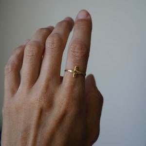 May include: A gold hammered cross ring. The ring is simple and delicate, with a small cross design.