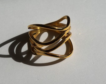 Può includere: Un anello dorato con un design unico, ondulato e multistrato. L'anello è in metallo e ha una finitura liscia e lucida.