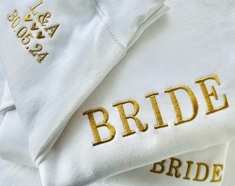 May include: White sweatshirt with gold embroidery that says "BRIDE" and "L&A 30.05.24" with small hearts.
