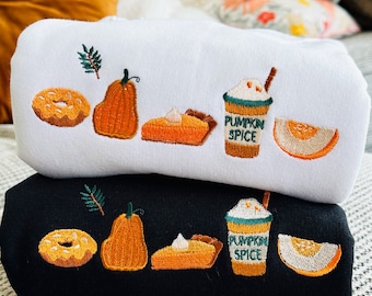 May include: Two black and white sweatshirts with embroidered fall-themed designs. The designs include a pumpkin, a slice of pie, a donut, a cup of pumpkin spice latte, and a slice of melon. The text on the cup reads "Pumpkin Spice".