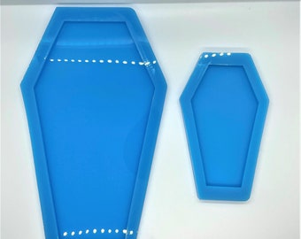 May include: Two blue silicone moulds shaped like coffins. The larger mould is about 15 cm long and the smaller mould is about 7.5 cm long.