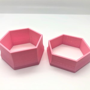 Puede incluir: Dos cortadores de galletas hexagonales de plástico rosa, uno más grande que el otro.