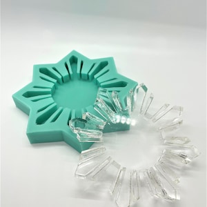 May include: A teal silicone mold shaped like a star with a raised design of a sunburst. A clear resin sunburst is sitting on top of the mold.