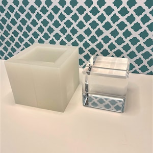 Op de afbeelding: Een witte siliconen mal en een transparante acryl kubus. De mal is rechthoekig en heeft een glad oppervlak. De kubus is transparant en heeft een glanzende afwerking.