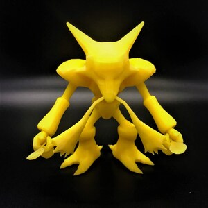 Puede incluir: Una figurita amarilla impresa en 3D de una criatura con cabeza de lobo, orejas largas y cola. La criatura tiene un cuerpo humanoide con brazos y piernas.