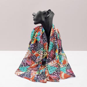 May include: A colorful scarf with a vibrant patchwork design. The scarf features a mix of patterns, including stripes, polka dots, and abstract shapes in shades of orange, blue, green, and purple. The scarf is draped over a black mannequin head.