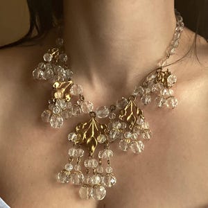 May include: A vintage necklace featuring clear crystal beads and gold-toned leaf-shaped pendants. The necklace has multiple strands of small, round beads and larger, faceted crystal drops. The gold pendants add a touch of elegance to the design.