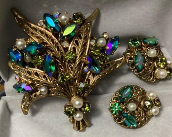 Peut inclure: Un ensemble de bijoux vintage de couleur dorée comprenant une broche florale et des boucles d'oreilles assorties. La broche et les boucles d'oreilles sont ornées de strass verts et bleus irisés, de petites perles blanches et d'accents verts.