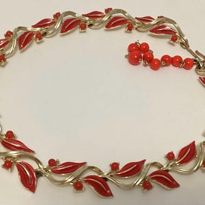 May include: A vintage necklace featuring a gold-tone metal design with red enamel leaf-shaped elements and small red bead accents. The necklace has a delicate, flowing design, with a hook clasp closure.