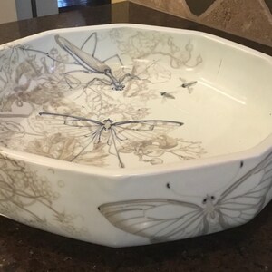 May include: White ceramic serving bowl with an octagonal shape. The bowl features grey illustrations of insects, butterflies, and foliage. The design wraps around the exterior and interior of the bowl.