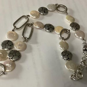 May include: A bracelet featuring alternating white coin-shaped pearls and circular silver-toned metal discs with a dotted pattern, connected by silver-toned oval links. The piece includes a silver-toned toggle clasp and an adjustable chain extension.