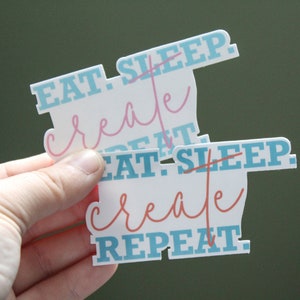 May include: Two white stickers with blue and pink text. The top sticker says "Eat. Sleep. Create. Repeat." The bottom sticker says "Eat. Sleep. Create. Repeat."