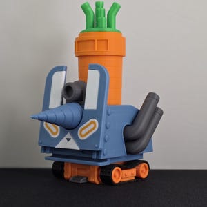 May include: A whimsical, 3D-printed toy robot in the shape of a bunny and carrot. The robot features a blue body, orange wheels and carrot-shaped top, and a drill-like nose. The toy is designed with a cartoonish aesthetic.