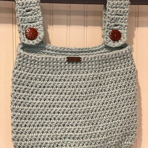 May include: A light blue crocheted hanging organizer with two straps and wooden buttons. The organizer has a small brown label with the word "Handmade" on it.