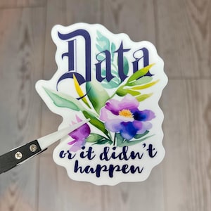 May include: A white sticker with the word "Data" in a dark blue, ornate font, and the phrase "or it didn't happen" in a similar font. The sticker features a floral design with purple and blue flowers and green leaves.
