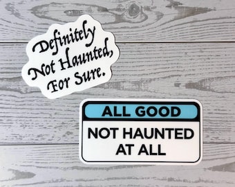 May include: Two white stickers with black text on a light wood grain surface. One sticker reads "Definitely Not Haunted, For Sure." in a whimsical font. The other sticker is rectangular with the text "ALL GOOD NOT HAUNTED AT ALL".