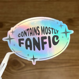 May include: A holographic sticker with a speech bubble shape and the text "CONTAINS MOSTLY FANFIC" in black lettering. The sticker has a rainbow iridescent finish and stars around the text.