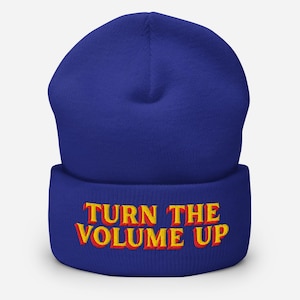 May include: A royal blue beanie with the embroidered text "TURN THE VOLUME UP" in yellow and red. The beanie is a classic, comfortable style, perfect for cold weather or casual wear.