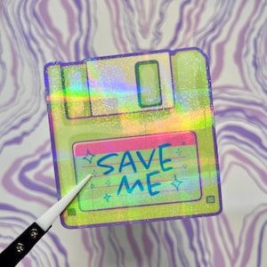 May include: A holographic sticker of a floppy disk with the text "SAVE ME" written on it. The sticker has a glittery, iridescent finish.