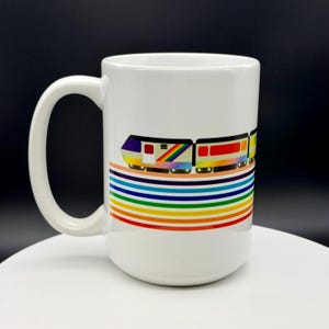 Puede incluir: Taza de cerámica blanca con un diseño de tren colorido y rayas arcoíris. Los vagones del tren son en tonos morado, amarillo, rojo y naranja. La taza tiene un asa grande y es adecuada para bebidas frías o calientes. Mide unos 12 cm de alto.