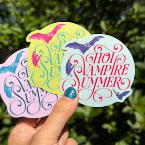 May include: Three circular stickers featuring the text HOT VAMPIRE SUMMER in decorative script. The stickers are light blue, yellow, and light purple, each displaying purple, pink, or blue bat illustrations flying and hanging from the lettering.