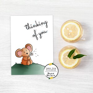 May include: A printable card with a cute cartoon mouse blowing on a dandelion. The card says "thinking of you" in a sparkly font. The card is on a white wooden background with two glasses of lemonade.