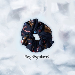 May include: A navy blue scrunchie with a gingerbread man and candy cane print. The text "Navy Gingerbread" is below the scrunchie.
