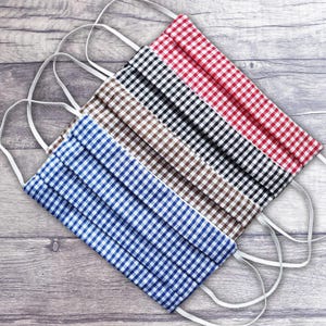 May include: Four fabric face masks with gingham patterns in blue, brown, black, and red. The masks are folded and have white elastic ear loops.
