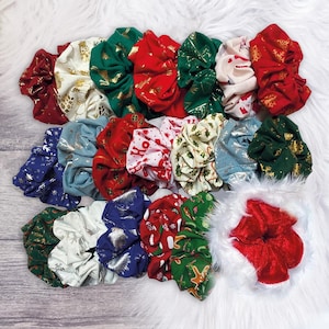 May include: A collection of 15 Christmas-themed scrunchies in various colors and patterns, including red, green, white, and gold. The scrunchies feature festive designs like snowflakes, reindeer, and Christmas trees.