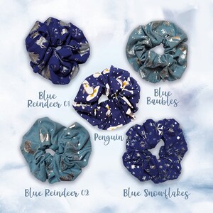 May include: Five blue and silver patterned scrunchies. The scrunchies feature different winter-themed designs, including penguins, reindeer, snowflakes, and baubles. The text "Blue Reindeer 01", "Blue Reindeer 02", "Penguin", "Blue Baubles", and "Blue Snowflakes" is printed below each scrunchie.