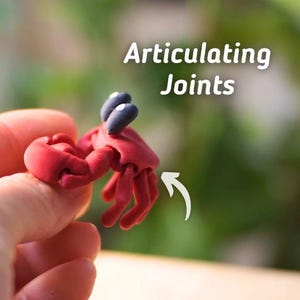 Puede incluir: Una figura de cangrejo rojo con ojos negros y articulaciones. La figura se sostiene en una mano, con el texto "Articulating Joints" en letras blancas en el fondo. El cangrejo tiene una superficie detallada y texturizada.