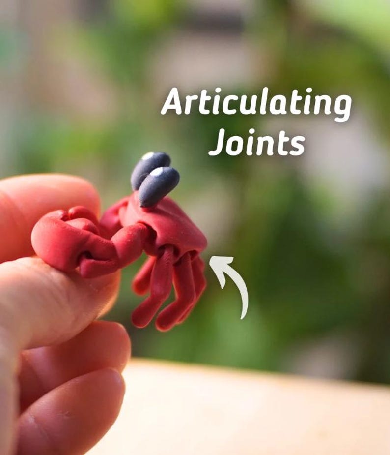 Puede incluir: Una figura de cangrejo rojo con ojos negros y articulaciones. La figura se sostiene en una mano, con el texto "Articulating Joints" en letras blancas en el fondo. El cangrejo tiene una superficie detallada y texturizada.