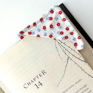May include: A floral fabric corner bookmark featuring red roses and blue flowers on a white background. The bookmark is placed on a book, with the text "CHAPTER 14" visible.