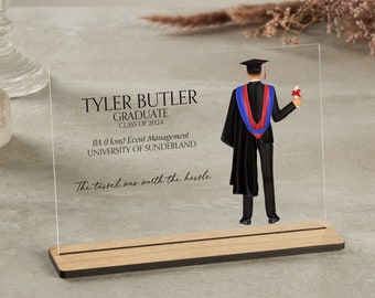 May include: A clear acrylic plaque with a black and white illustration of a graduate holding a diploma. The text on the plaque reads "Tyler Butler Graduate Class of 2024 BA (Hons) Event Management University of Sunderland The tassel was worth the hassle."