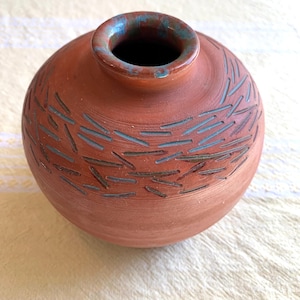 May include: A terracotta vase with a round body and a blue and brown rim. The vase has a decorative pattern of blue lines etched into the surface.