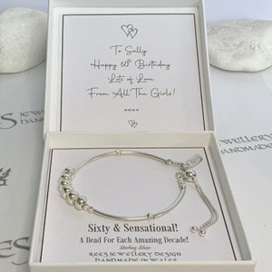 May include: A silver bracelet with a charm that says "Rees" and a message that reads "Sixty & Sensational! A Bead For Each Amazing Decade! Sterling Silver Rees Jewellery Design Handmade in Wales".