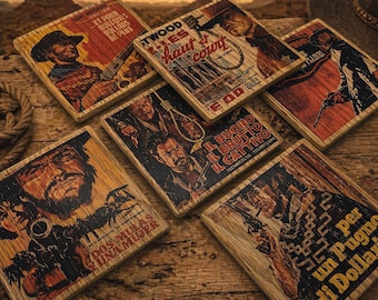 May include: A collection of square wooden coasters featuring vintage movie posters with Western themes. The coasters display images of cowboys, guns, and text in various languages, set against a rustic wooden background. The color palette includes browns, reds, and yellows.
