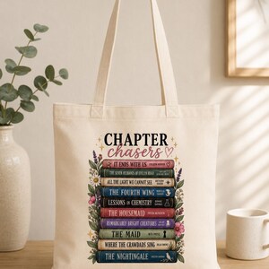 May include: A cream-colored canvas tote bag featuring a graphic print of a stack of books with the text "CHAPTER chasers" at the top. The design includes colorful floral accents on both sides of the book stack and various book titles.