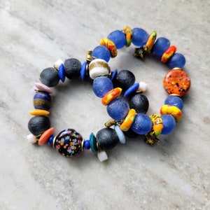 May include: Two bracelets made of colorful glass beads. One bracelet is blue, orange, and yellow. The other bracelet is black, blue, orange, and white.